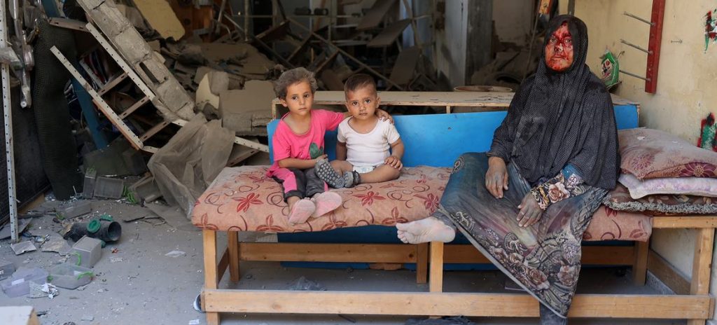 junio © UNICEF Una mujer y sus hijos se sientan dentro de su casa destruida en Burij en el centro de la Franja de Gaza.